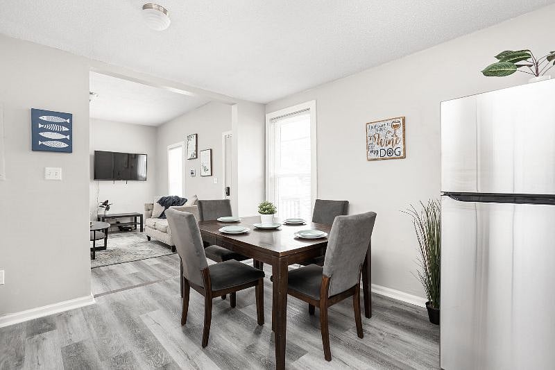 Modern open-concept dining and living area featuring a sleek wooden dining table with plush gray chairs, stylish decor accents, and a cozy living space seamlessly connected in a bright, airy setting.