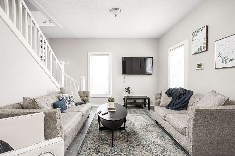 Stylish and cozy living room featuring matching neutral-toned sofas, a patterned area rug, and a sleek black coffee table, all set beneath a wall-mounted TV and accented by minimalist wall art.