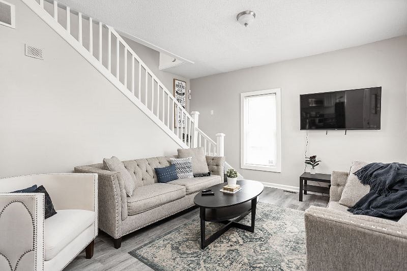 Contemporary living room with a chic neutral color palette, featuring tufted sofas, a stylish armchair, a sleek black coffee table, and a wall-mounted TV, all set against a backdrop of soft natural light and a modern staircase
