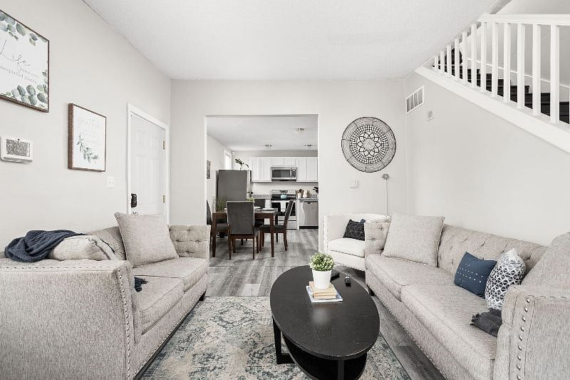 Bright and inviting open-concept living space featuring plush neutral-toned sofas, a stylish black coffee table, and modern decor, seamlessly flowing into a contemporary kitchen and dining area.