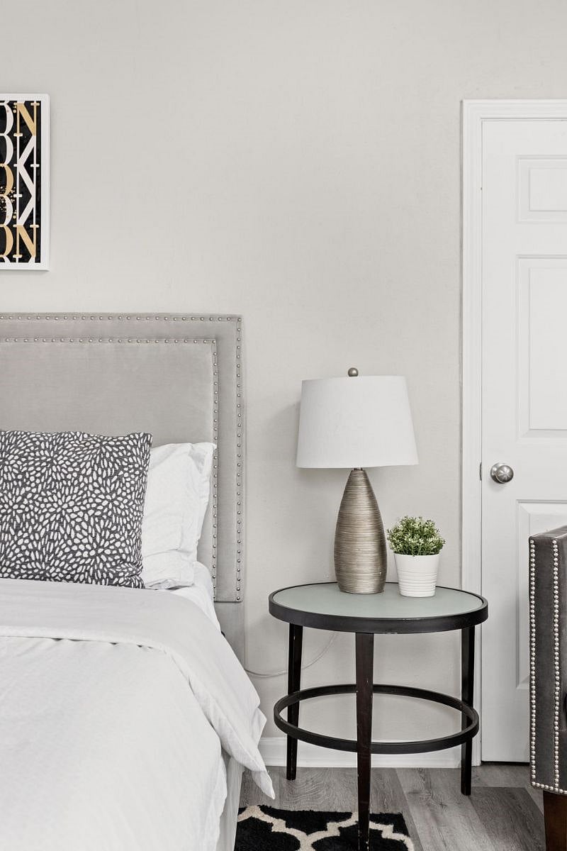 Cozy and stylish bedroom corner featuring a tufted headboard, patterned throw pillows, and a sleek bedside table with a modern lamp and a small potted plant for a touch of greenery.