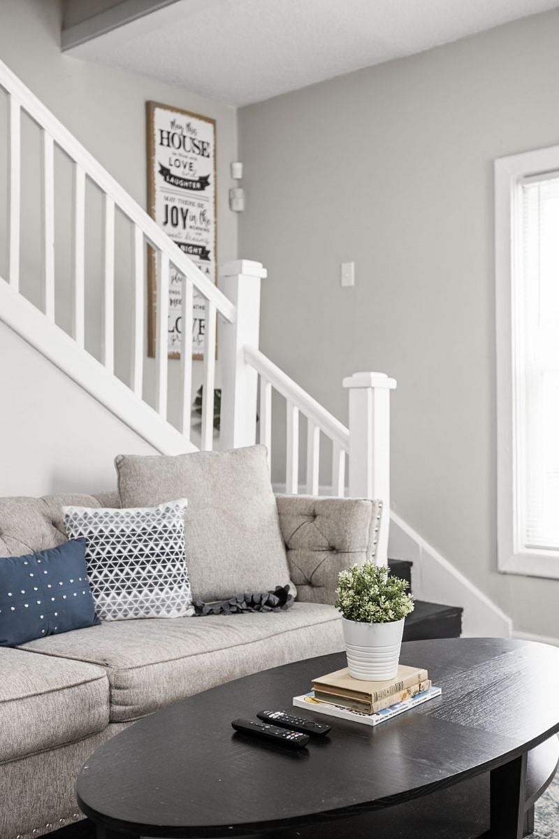 A cozy and modern living area featuring a tufted sofa with decorative pillows, a sleek white staircase, and soft neutral tones that create a welcoming and stylish atmosphere.