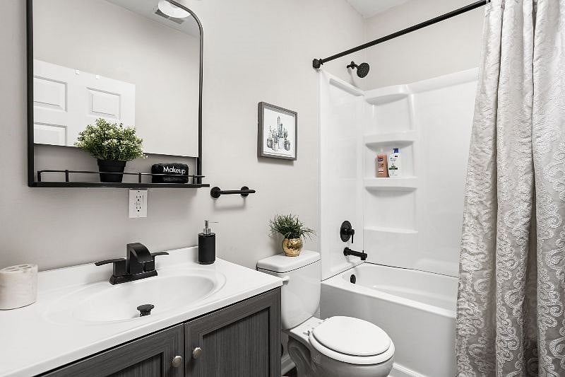 Stylish and modern bathroom featuring a sleek vanity with black hardware, a large mirror with shelf, a white tub with built-in shelving, and elegant black fixtures, all complemented by minimalistic decor and a patterned shower curtain.