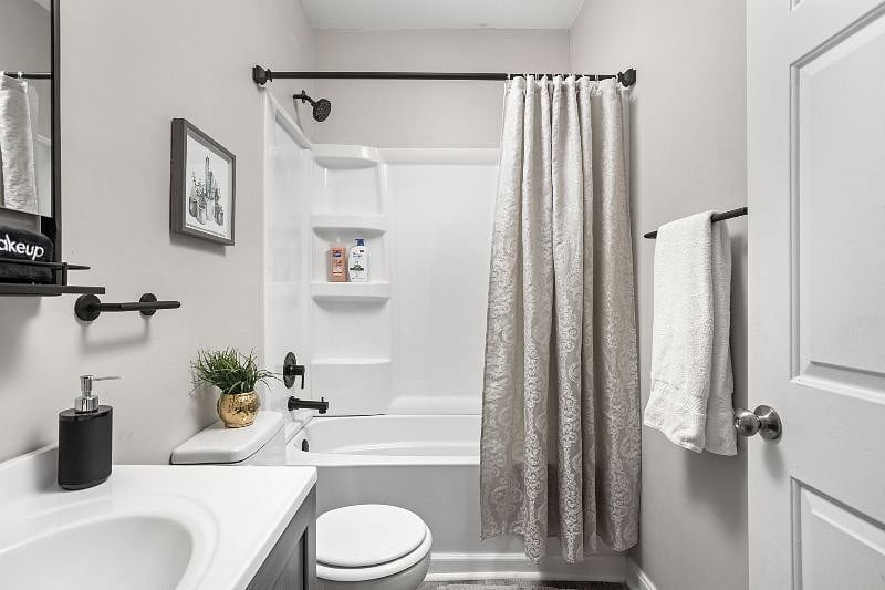 Modern and clean bathroom featuring a white bathtub with built-in shelving, a sleek vanity with black fixtures, a patterned shower curtain, and subtle decorative touches for a fresh, stylish look.