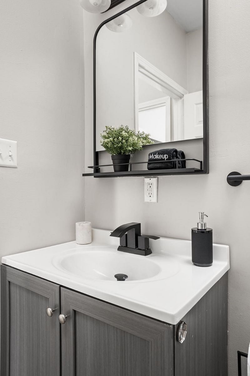 A sink and mirror accompanied by a vanity cabinet and provided soap.