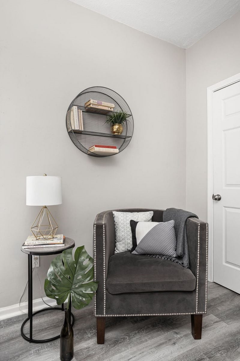 Cozy and stylish reading nook featuring a studded armchair with decorative pillows, a modern geometric lamp on a side table, and a circular wall shelf with books for a chic finishing touch.