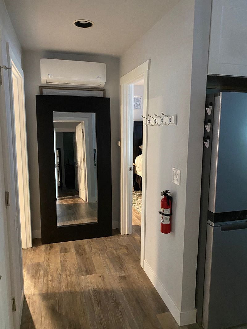 hallway with large mirror. To the right is the entry to the living/kitchen area; to the left is the entry into the bathroom, and to the far right is the entry into the bedroom.
