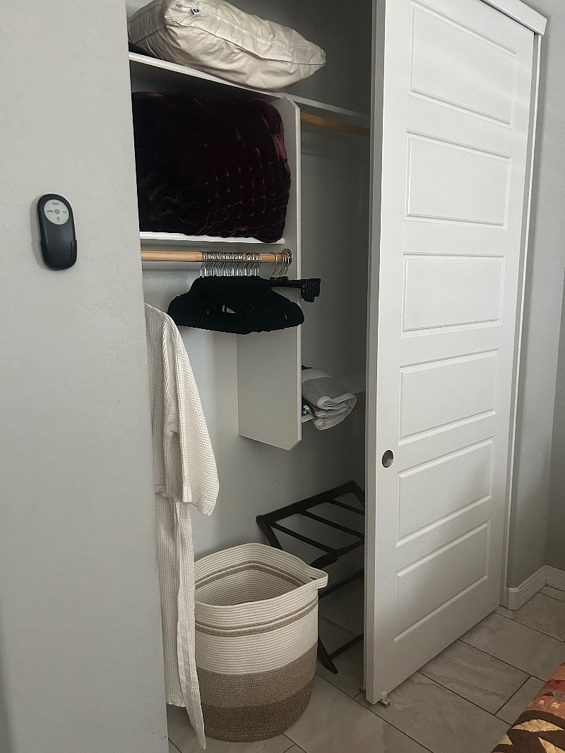 The closet has robes, hangers, shelves, a suitcase stand, a laundry basket and a pool towel