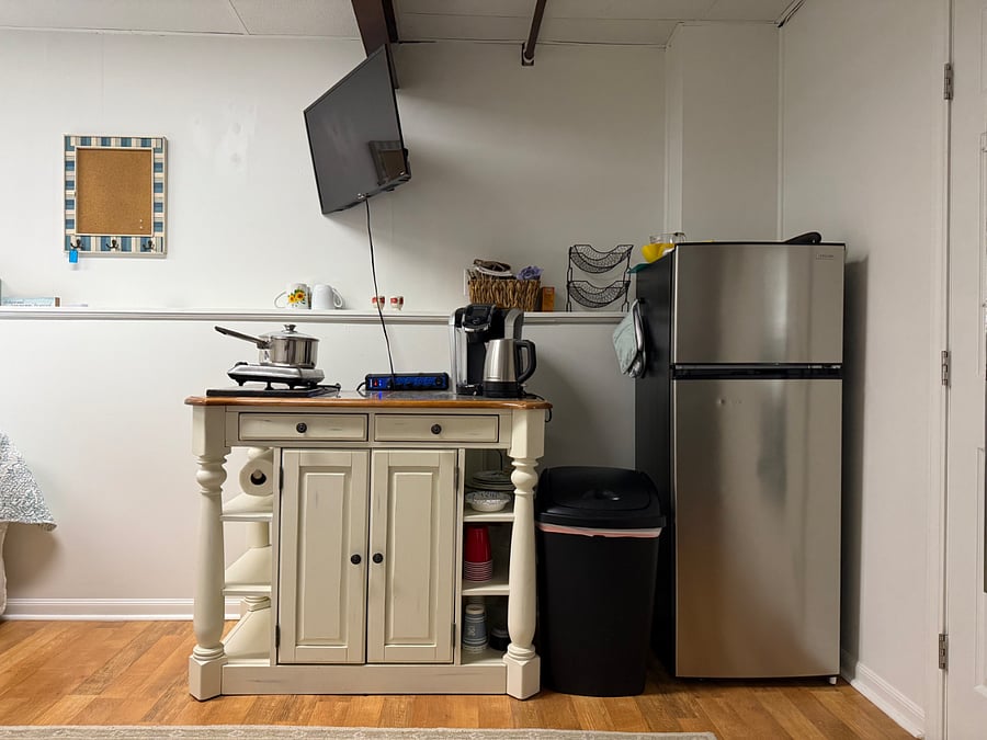Stocked kitchenette with a full-sized refrigerator, hot plate, hot kettle, Keurig machine, microwave, and toaster oven. There are utensils, plates, bowls, and cups as well.