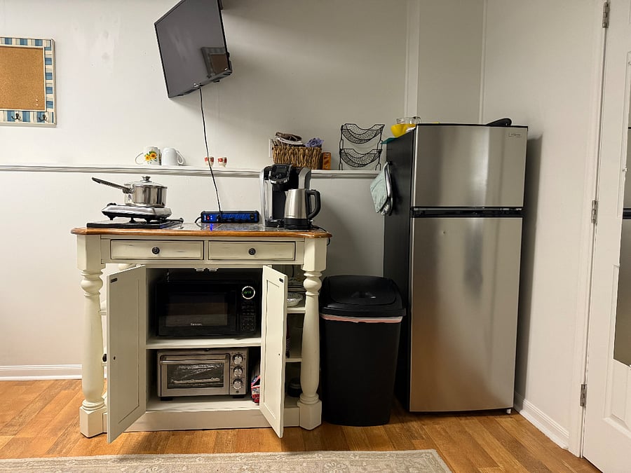 Stocked kitchenette with a full-sized refrigerator, hot plate, hot kettle, Keurig machine, microwave, and toaster oven. There are utensils, plates, bowls, and cups as well.