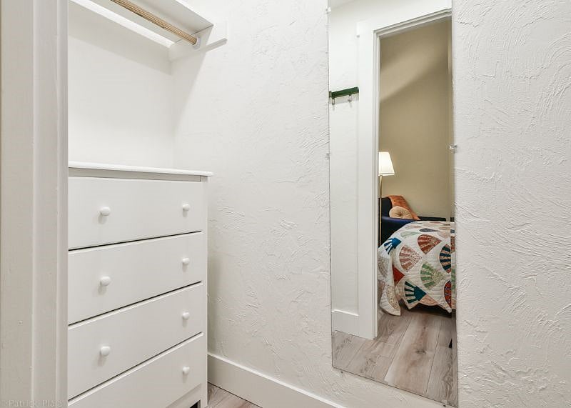 Closet with lights, mirror, dresser and plenty of room for hanging clothes with hangers as well as a laundry basket.