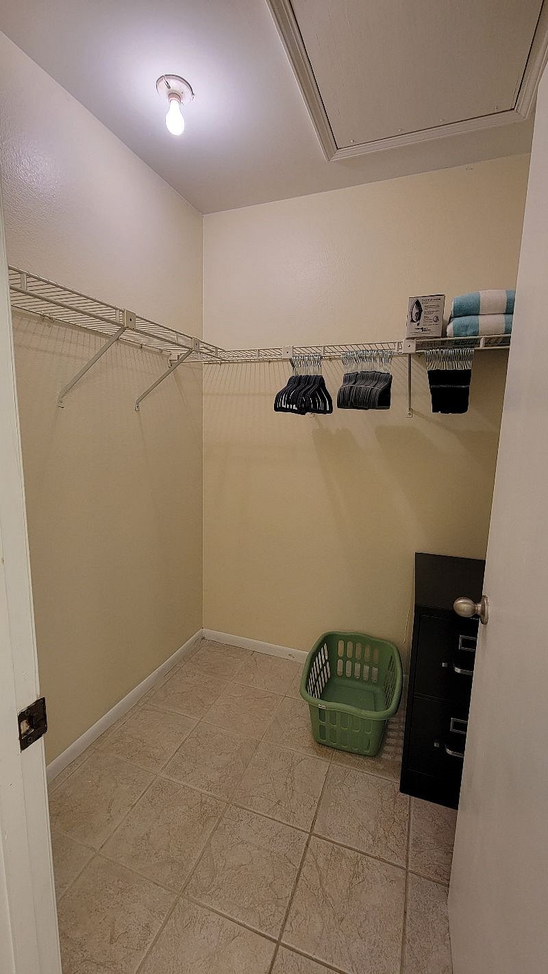 Large walk-in closet with a clothes hamper and lots of felt hangers.