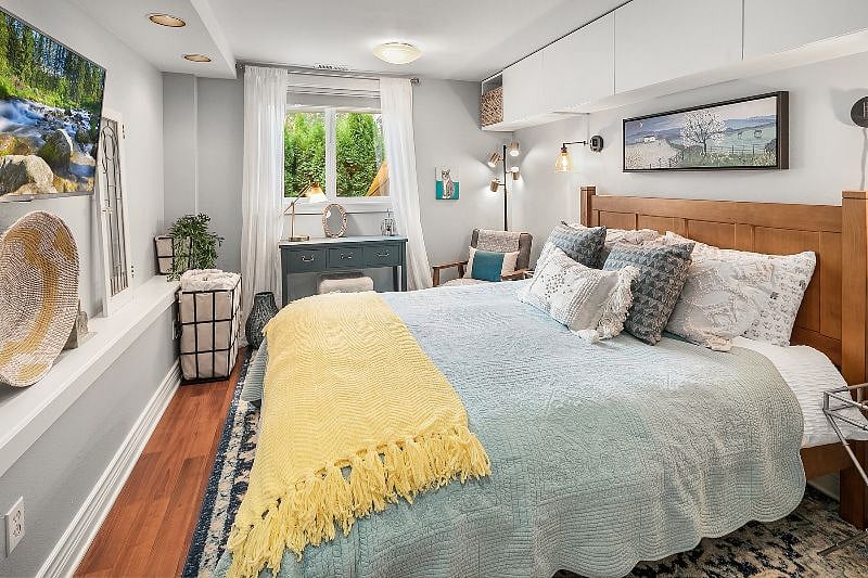 Blue bedroom with queen sized bed (linens/blankets for all seasons), writing desk, dressing chair, bedside tables on both sides with wall sconces, closet with hanging rod and full-sized 6 drawer wooden dresser, wall mounted 42" LG smart TV, and above bed storage. Cellular blinds for room darkening