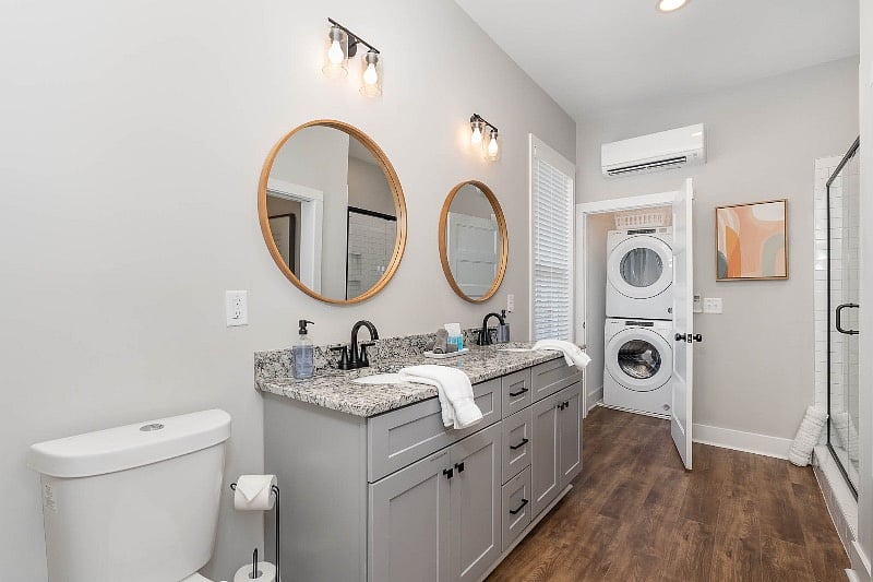 Large full bathroom with tiled walk-in shower, dual sink vanity, and washer and dryer closet. The bathroom is accessible directly from the bedroom or from the hallway for guests.