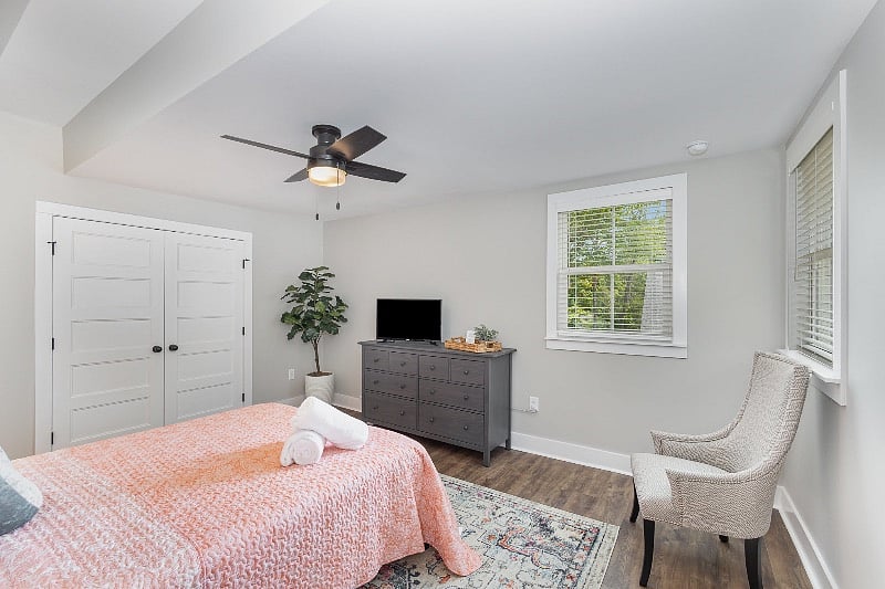 Large bedroom with queen-sized mattress, ceiling fan, large closet, dresser and TV.