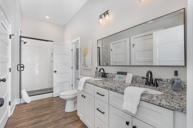 Spacious bathroom with dual-sink vanity, tiled, walk-in shower, full-sized washer and dryer, and additional utility storage. Direct entrances from both bedroom and hallway for extra privacy.