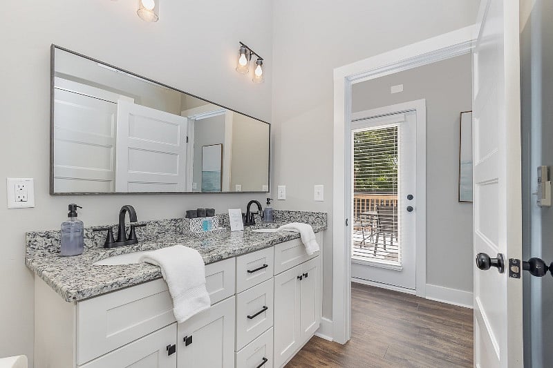 Spacious bathroom with dual-sink vanity, tiled, walk-in shower, full-sized washer and dryer, and additional utility storage. Direct entrances from both bedroom and hallway for extra privacy.