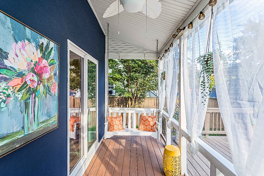That porch swing with playful orange pillows is perfect for lazy mornings or evening conversations. The string lights create ambiance while you overlook the fenced backyard and large trees.