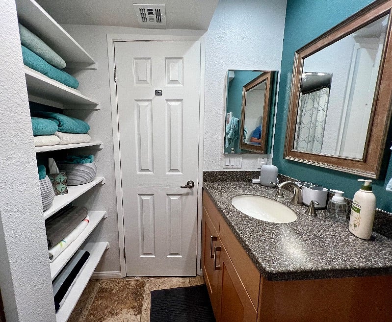 The second bathroom is across from the second bedroom and next to the living/dining area. It features a walk-in shower, ample under-sink storage, and shelving behind the door.