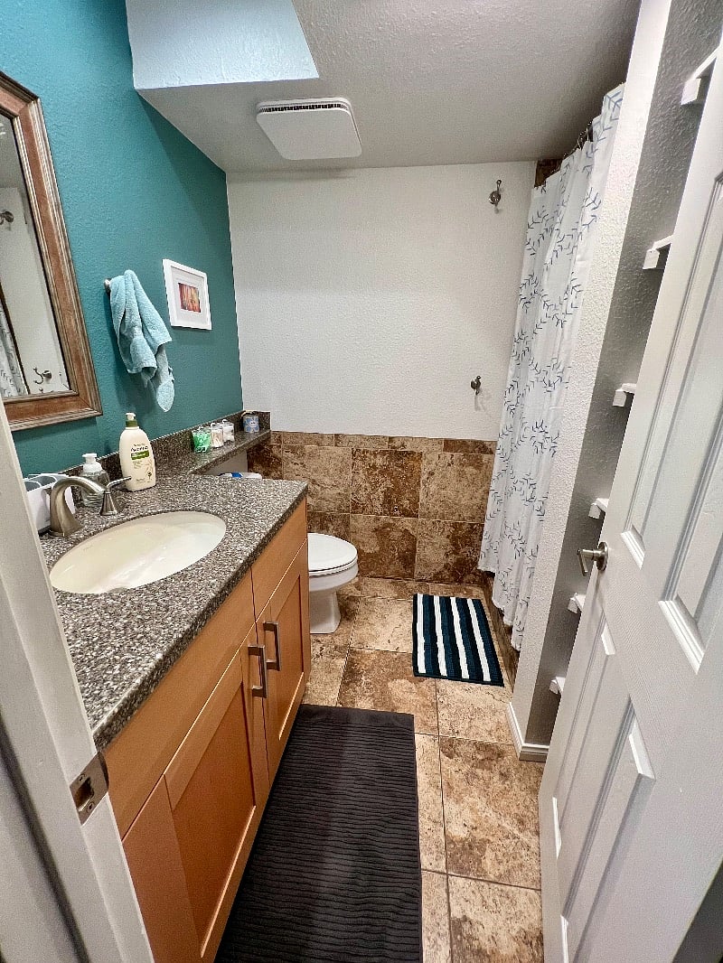 The second bathroom is across from the second bedroom and next to the living/dining area. It features a walk-in shower, ample under-sink storage, and shelving behind the door.