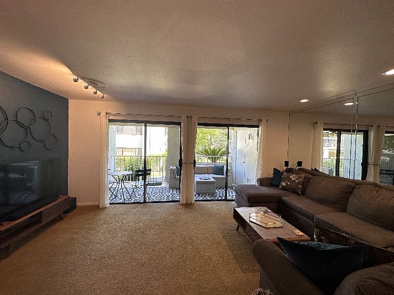 The living room includes a 4K Samsung smart TV with an Apple TV and surround sound. It connects seamlessly with the outdoor patio, which includes a small bistro set and a sectional outdoor couch.