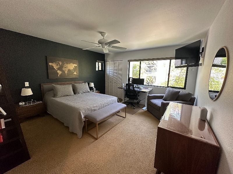 The corner primary suite offers an ensuite bath, an armchair, wall-mounted 50-inch HD TV with sound bar + Apple TV and workspace with standing desk with plenty of storage in a large dresser, two nightstands, and an in-room closet.