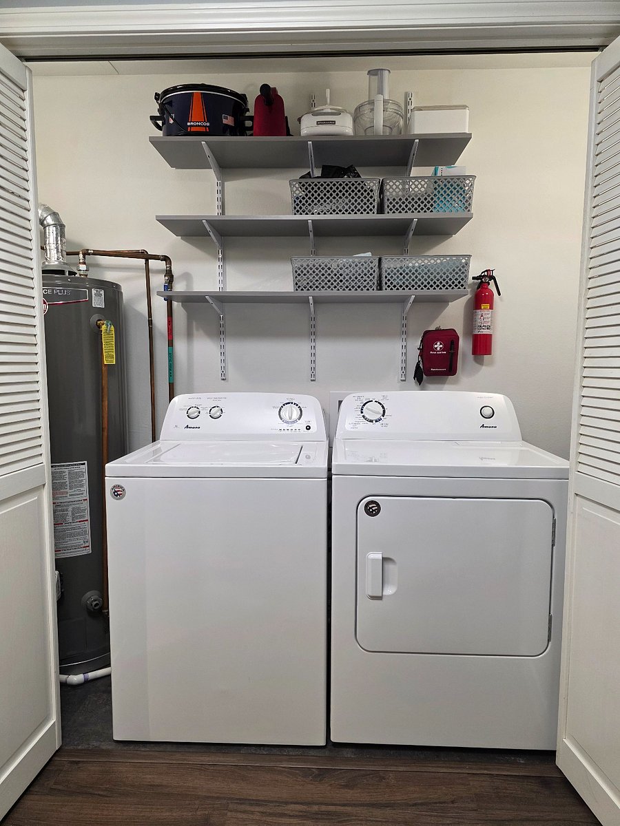 Washer and dryer in utility closet in kitchen. A variety of amenities and small kitchen appliances are located above. Cleaning supplies, extra light bulbs, and reusable grocery bags can be found to the right.