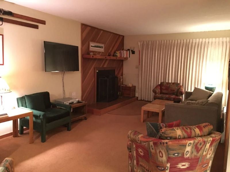 Living room with working wood fireplace, and glass all the way across behind the curtains and deck entrance.