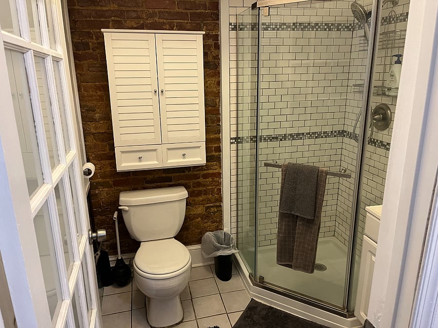 Bathroom with newly tiled shower, vanity, and storage over toilet and vanity. Lots of light from large window.