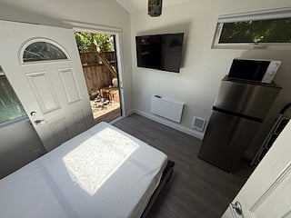 a bit of an aerial view showing bed when in open position, flat screen smart tv, folding table desk under tv, part of refrigerator and microwave. door opened to patio.