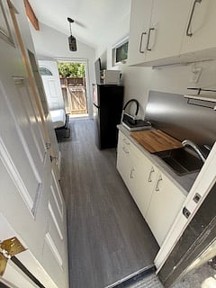entering cottage. kitchenette with full cabinets, sink, cutting board, granite, step stool to reach high cabinets. to the left is bathroom.