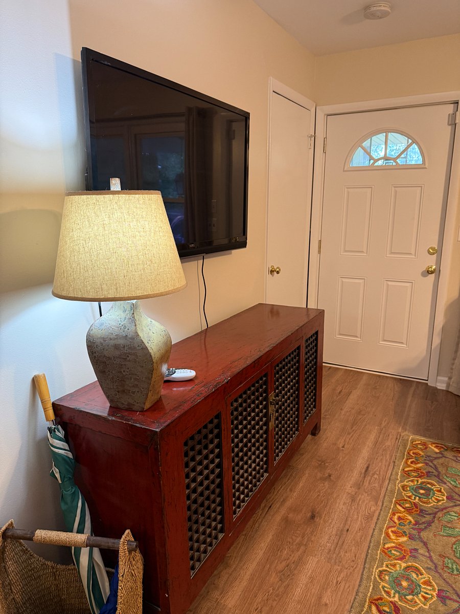 Living room area with TV mounted on wall. coat close, comfy couch and chairs. 