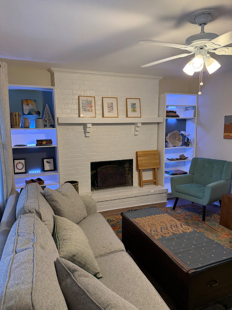 Living room area with TV mounted on wall. coat close, comfy couch and chairs.