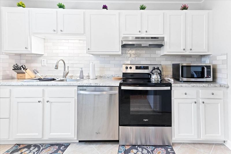 Kitchen with new range, hood, cabinets, counters, microwave, and backsplash.