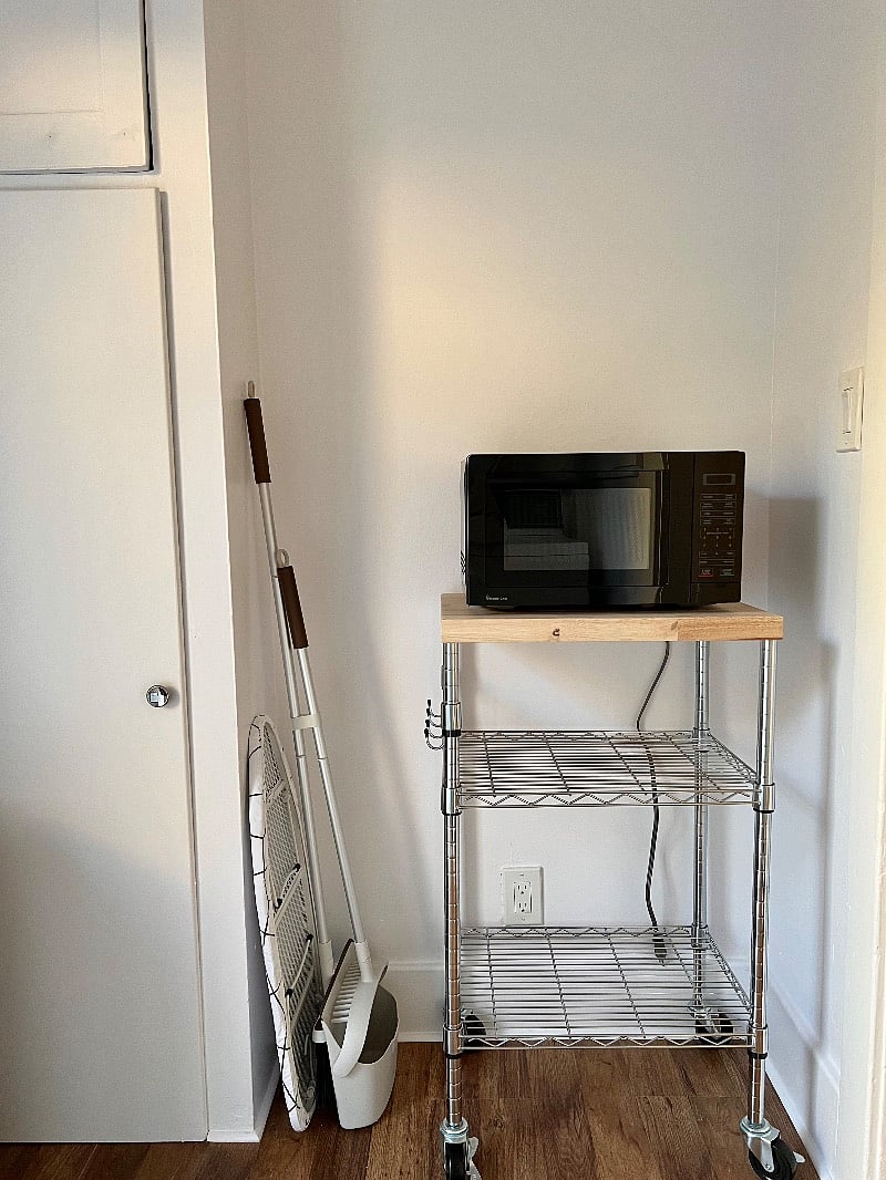 Utility room with microwave, laundry detergent, portable fan and heaters, iron/ironing board, broom. 