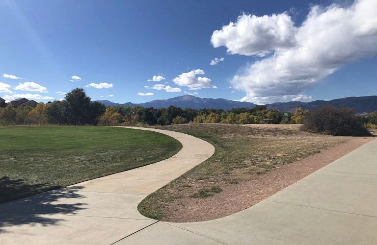Cottonwood Creek park track. In the background is a bench. This is next to a launch pad for the park's 18 basket disc golf course.
