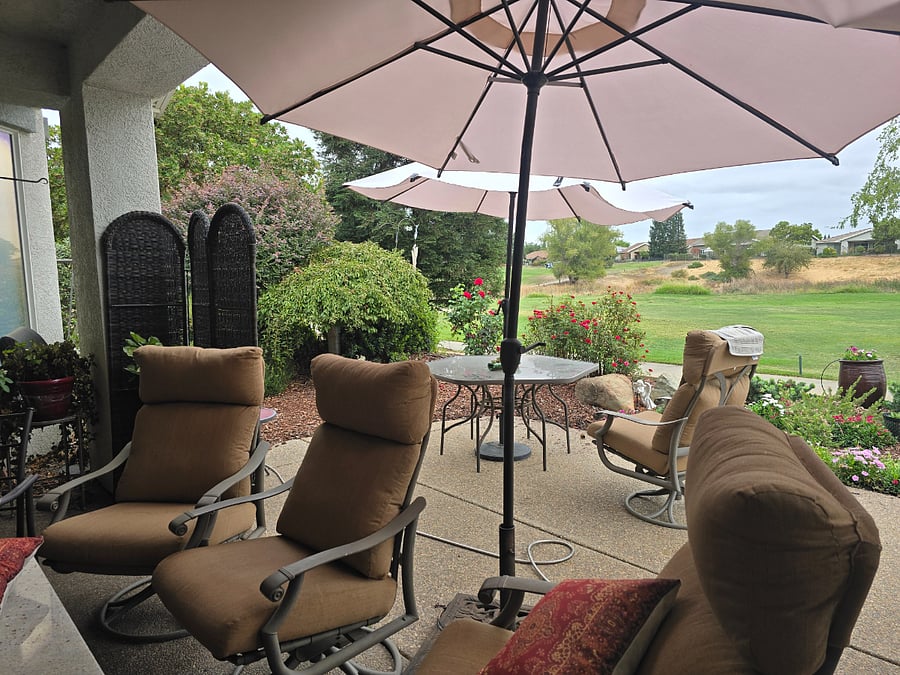 Home on golf course with many flowers in large furnished patio.