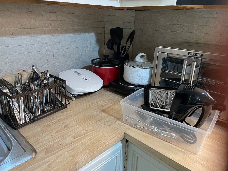 Here are more kitchen appliances: Mini crockpot, countertop, grill, a stovetop eye with a pot, silverware, a mini oven that is also an air fryer and toaster.