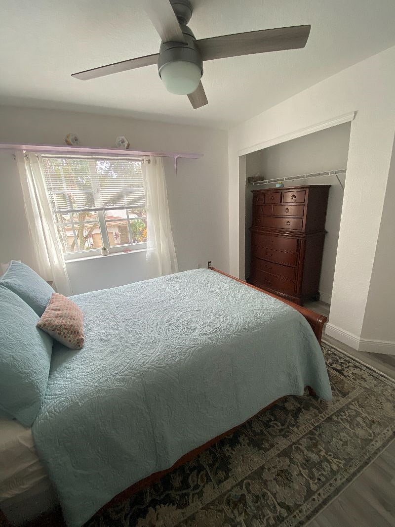 A full size dresser, desk, chair, full size bed with nightstand. A small refrigerator is located in the room.