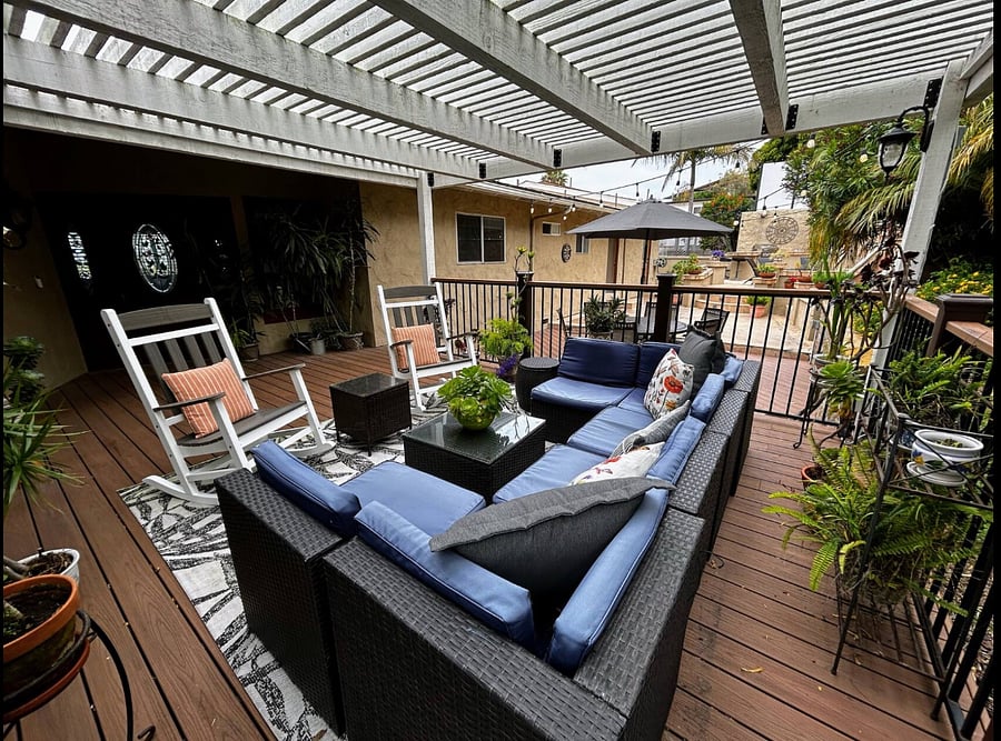 View from the Gazebo to the outdoor patio area that has dining table for 6, patio lights, outdoor fire pit and kitchen with gas BBQ, small fridge and sink.