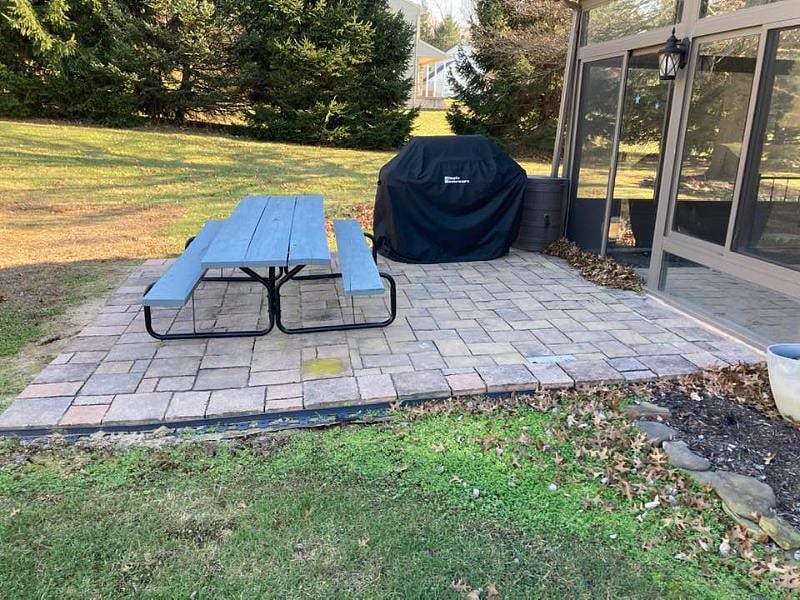 Picnic table and gas grill on patio, joined to enclosed patio.