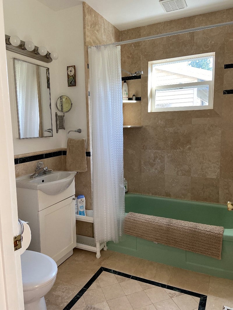 full bathroom with marble tile floor, vintage green tub, and bright vanity lighting, magnifying shaving mirror. Unscented conditioner and shampoo available.