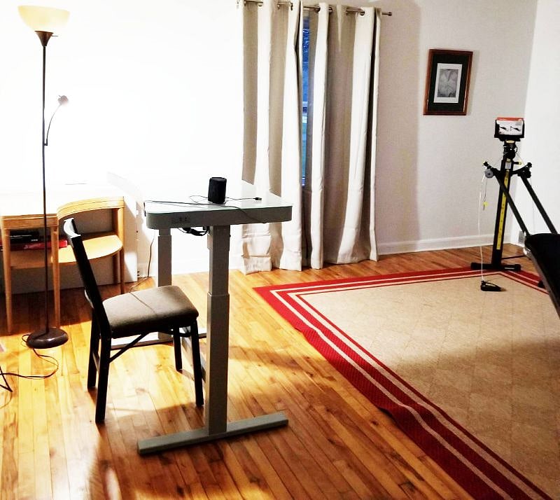 Living room converted into an office with adjustable height desk and a total gym.