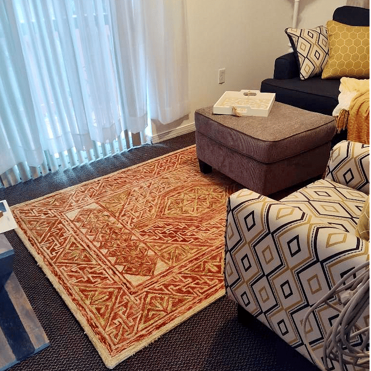 Bright and airy living room designed for comfort and relaxation. Features include a cozy sofa, club chair, ottoman, and a floor lamp for ambient lighting. A ceiling fan keeps the space cool and breezy, while the smart TV makes it easy to stream your favorite shows during downtime.