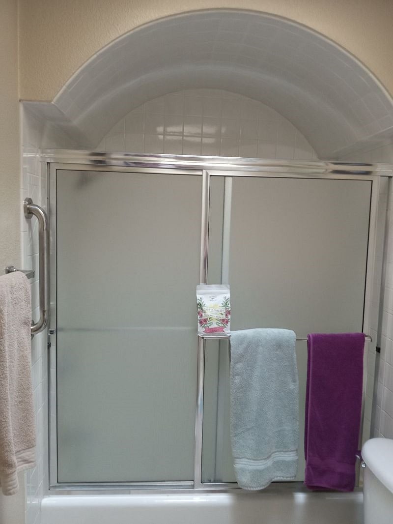 Bathroom shower and bathtub with sliding doors and fresh clean towels ceramic tile floor and new toilet with large mirror and vanity lights.