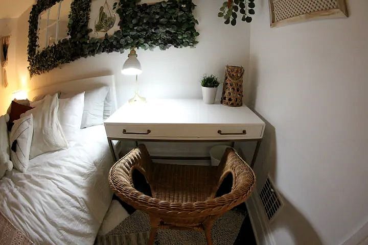 The larger bedroom is decorated in a boho chic style with verdant plant life and light, airy colors. It also has a dedicated workspace.
