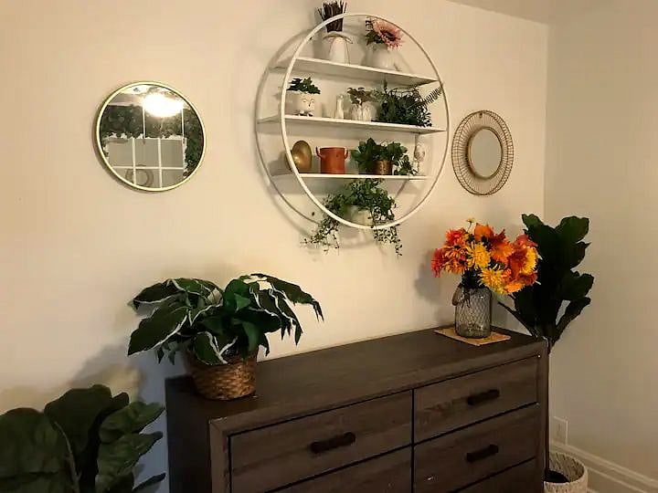 The larger bedroom is decorated in a boho chic style with verdant plant life and light, airy colors. It also has a dedicated workspace.