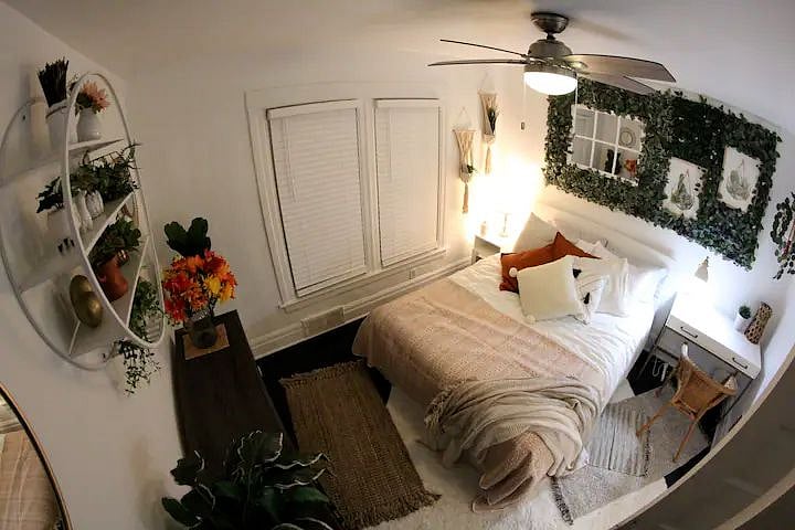 The larger bedroom is decorated in a boho chic style with verdant plant life and light, airy colors. It also has a dedicated workspace.