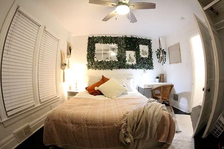 The larger bedroom is decorated in a boho chic style with verdant plant life and light, airy colors. It also has a dedicated workspace.