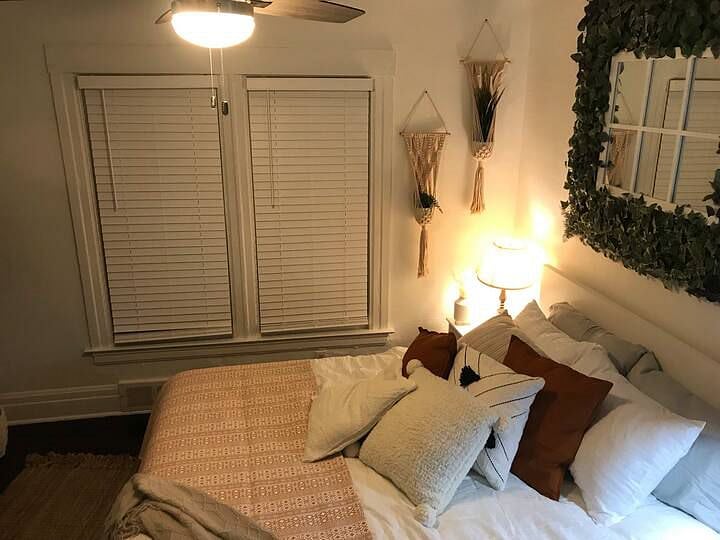 The larger bedroom is decorated in a boho chic style with verdant plant life and light, airy colors. It also has a dedicated workspace.